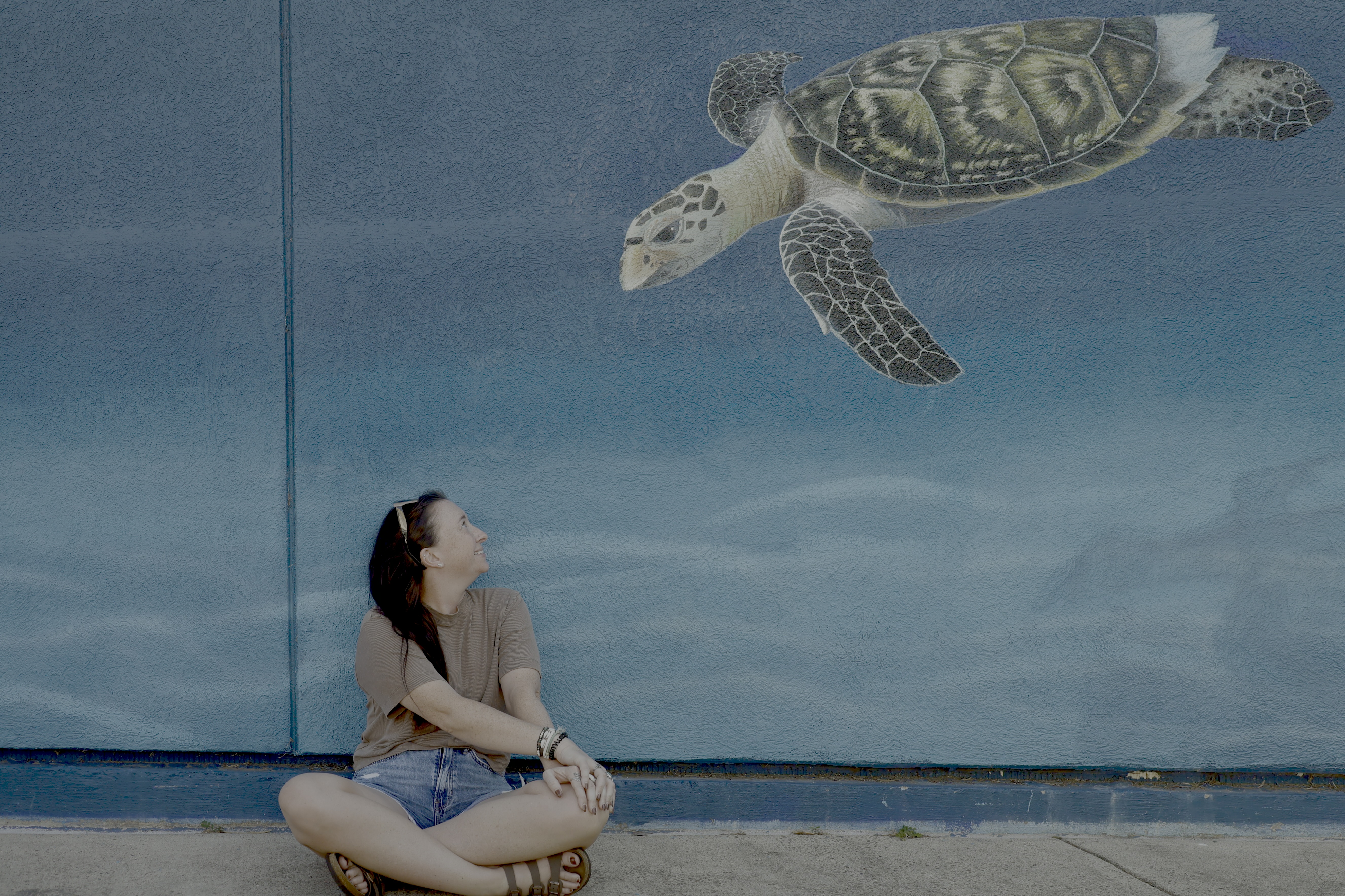 Hannah Yarbrough sitting beneath a sea turtle mural in Port Aransas